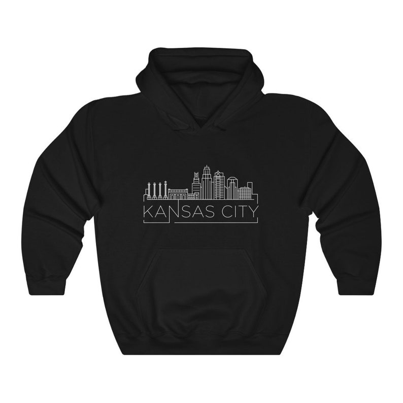 Może przedstawiać: Czarna bluza z kapturem z białym rysunkiem linii panoramy Kansas City. Nazwa miasta jest wydrukowana na dole na biało. Bluza ma przednią kieszeń i kaptur ze sznurkiem.