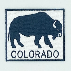 May include: A white embroidered patch with a dark blue silhouette of a buffalo and the word "COLORADO" underneath.