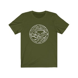 May include: A green t-shirt with a white outline of the state of Tennessee seal. The seal features a mountain range, a river, and the words "Agriculture and Commerce".
