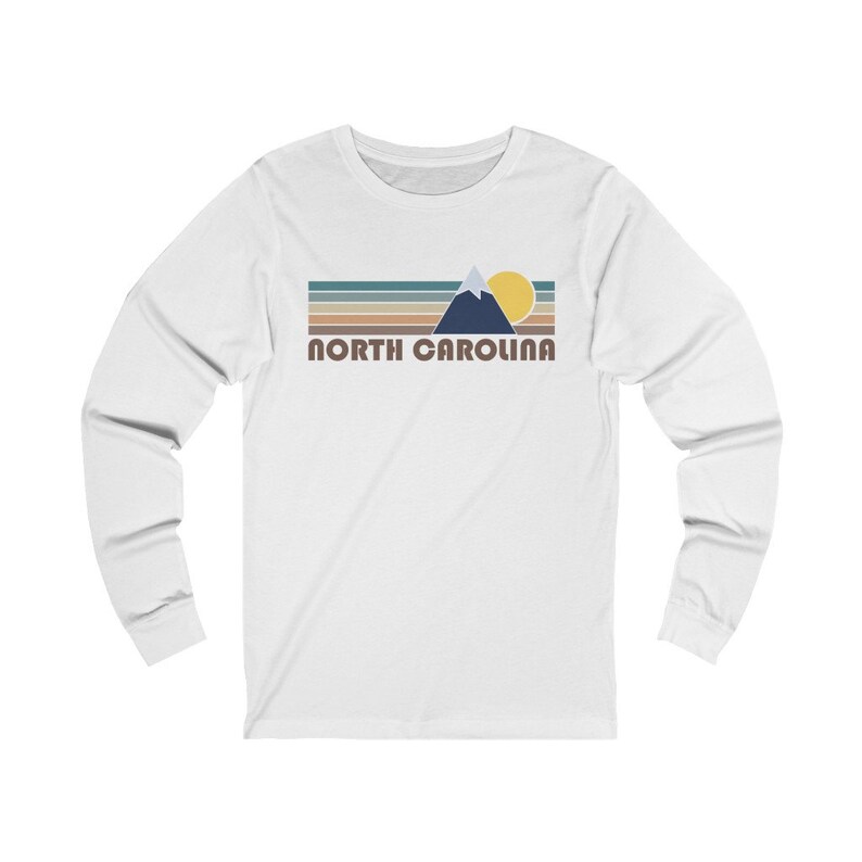 May include: White long-sleeve t-shirt with a retro-style graphic of a mountain range, sun, and the text "NORTH CAROLINA".