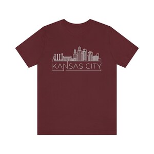 May include: A maroon t-shirt with a white outline of the Kansas City skyline and the text "KANSAS CITY" underneath.