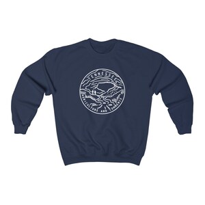 May include: Navy blue sweatshirt with a white graphic of the Tennessee state seal. The seal features a mountain range, a river, and the words "Agriculture and Commerce".
