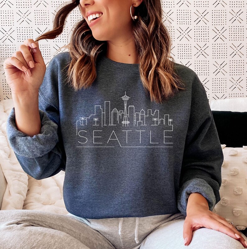 May include: A dark blue sweatshirt with a white outline of the Seattle skyline and the word "SEATTLE" underneath.