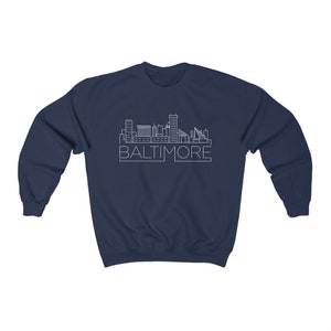 May include: Navy blue sweatshirt with a white outline of the Baltimore skyline and the word "BALTIMORE" underneath.