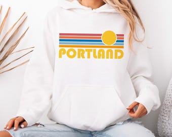 May include: White hoodie with a retro sunset graphic and the word "PORTLAND" in yellow.