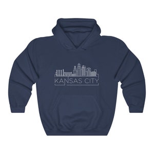 Może przedstawiać: Granatowa bluza z kapturem z białym rysunkiem linii horyzontu Kansas City. Nazwa miasta jest wydrukowana na dole na biało. Bluza ma przednią kieszeń i kaptur ze sznurkiem.