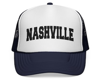 May include: A trucker hat with a white front panel and a navy blue brim and mesh back. The word "NASHVILLE" is printed in bold, black letters across the front of the hat.