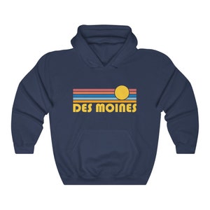 May include: Navy blue hooded sweatshirt with a retro sunset graphic and the text "DES MOINES" in yellow.
