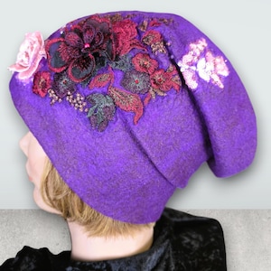 May include: A vibrant purple beanie hat with elaborate floral embroidery in shades of pink, burgundy, and green. The hat features a soft, textured fabric and a delicate pink rose accent.