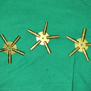 以下が含まれることがあります： 中央の円盤から放射状に伸びる円筒形のアームを持つ、真鍮色の星型のオブジェクトが3つ。各オブジェクトには、等間隔に配置された一連のアームがあります。オブジェクトは緑色の表面に配置されています。