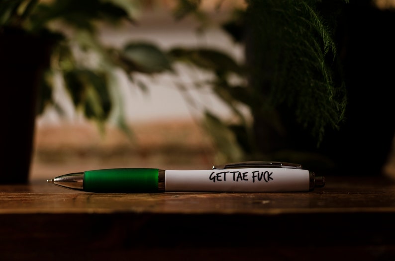 Puede incluir: Un bol&iacute;grafo blanco con un cuerpo verde y el texto "GET THE FUCK" escrito en &eacute;l.