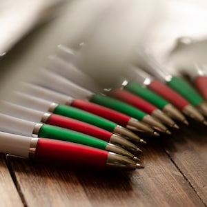 Puede incluir: Primer plano de un grupo de bol&iacute;grafos con detalles rojos y verdes. Los bol&iacute;grafos est&aacute;n dispuestos en fila, con las puntas apuntando hacia el lado derecho de la imagen. Los bol&iacute;grafos est&aacute;n sobre una superficie de madera.