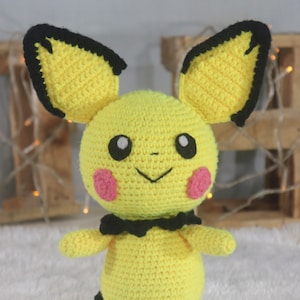 May include: A crocheted yellow Pikachu plush toy with black ears and a black bow tie. The toy has pink cheeks and black eyes.