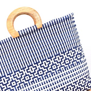 May include: A woven tote bag with a wooden handle. The bag has a blue and white geometric pattern. The handle is light brown. The bag is made of a sturdy material and is suitable for carrying various items.