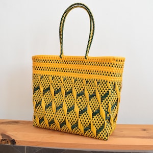 May include: A rectangular tote bag constructed from woven plastic strips in vibrant yellow and dark green. The bag features a repeating geometric diamond pattern throughout the body, a solid yellow top border, and two matching woven handles.