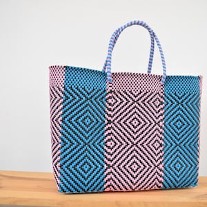 May include: A blue and pink woven tote bag with a geometric pattern. The bag has a light blue handle.