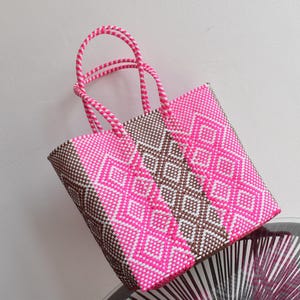May include: A pink and brown woven tote bag with a geometric pattern. The bag has two handles and is made of a sturdy material.