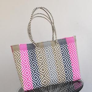 May include: A large, woven tote bag with a geometric pattern in pink, white, black, and gold. The bag has two handles.