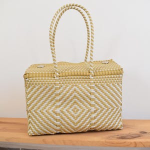 May include: A woven tote bag in a geometric pattern of gold and white. The bag has two handles and a rectangular shape. The bag is made of a durable, woven material, perfect for carrying items.