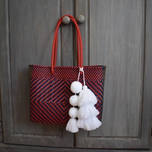 May include: A red and blue woven tote bag with white pom-poms hanging from the handles.