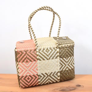 May include: Woven tote bag with a geometric pattern in pink, beige, and brown. The bag has a rectangular shape, a handle, and a lid. It's made of a durable material and is suitable for carrying items. The bag is approximately 30 cm in height.