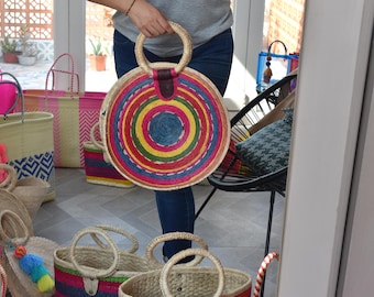 Può includere: Una collezione di borse di paglia intrecciata colorate, con forme rotonde e rettangolari. Le borse hanno manici in pelle e sono decorate con strisce e motivi colorati.