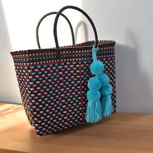 May include: A black and blue woven tote bag with a blue pom-pom tassel. The bag has a geometric pattern and is made of a sturdy material.