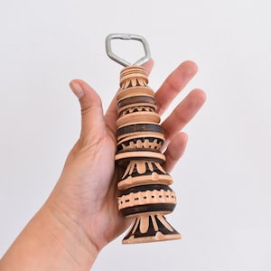 May include: A wooden bottle opener with a metal top. The opener is decorated with black and brown geometric patterns.