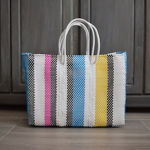 May include: A large, striped tote bag with handles. The bag is made of woven plastic and has a white background with black, pink, yellow, and blue stripes.