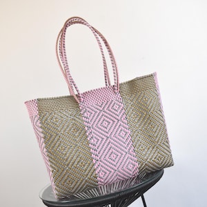May include: A large woven tote bag with pink, gold, and gray geometric patterns. The bag has two long handles.