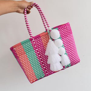 Peut inclure: Un sac cabas rayé rose, vert et orange avec des pompons et des glands blancs.