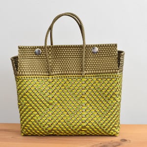 May include: A woven tote bag with a structured design. The bag features a two-tone pattern, with a yellow and green lower section and a solid olive green upper section. The bag has two handles and is secured with two silver press studs.