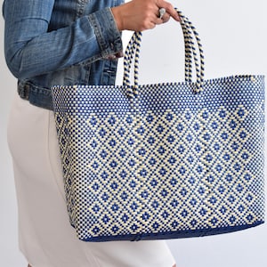 May include: A large, woven tote bag in navy blue and cream. The bag features a geometric diamond pattern and sturdy handles. The bag is made of a durable material and is suitable for carrying groceries or other items.