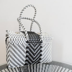 May include: A black and white woven tote bag with a black and white braided handle. The bag has a geometric pattern.