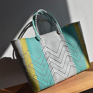 May include: A woven tote bag with a white, green, and yellow chevron pattern. The bag has two handles and is made of a plastic material.