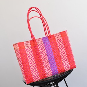 May include: A large pink and white woven tote bag with purple stripes. The bag has a geometric pattern and double handles.