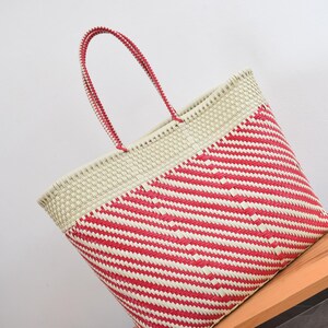 May include: A woven tote bag featuring a diagonal striped pattern in bright red and off-white. The bag has a solid off-white upper section and two matching red and white woven handles. The construction consists of tightly interlaced plastic strips.