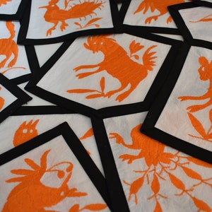 May include: A set of orange embroidered coasters with black borders. Each coaster features a different stylized animal design.
