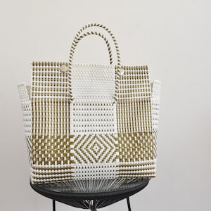 May include: A woven tote bag featuring a geometric pattern in white and olive green. The bag has two rounded handles and a structured rectangular body with a repeating diamond motif across the front panel, constructed from durable plastic strips.
