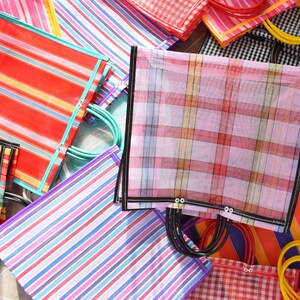 May include: A selection of brightly coloured tote bags with striped and checked patterns. The bags display a variety of colours, including red, orange, blue, purple, and yellow. The handles are made of plastic and come in various colours. The bags are made of a woven material.