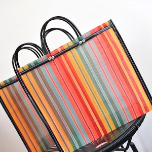 May include: Two colourful striped tote bags with black handles. The bags feature vertical stripes in red, orange, yellow, green, and blue. The bags are made of a woven material and have black trim.
