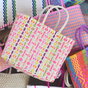 May include: A selection of brightly coloured woven tote bags. The bags display a variety of vibrant hues, including pink, yellow, green, and blue. Each bag has a woven pattern and strong handles, ideal for carrying items. The bags are made of a durable material.