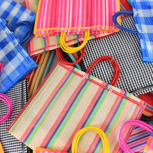 May include: A selection of brightly coloured, striped tote bags with matching handles. The bags display various colour combinations, including pink, blue, orange, and green stripes. Some bags have gingham patterns. The handles are in vibrant colours.