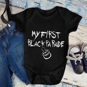 May include: Black bodysuit with white text that reads "My First Black Parade" and a pacifier graphic. The bodysuit is paired with blue denim shorts and black suspenders.
