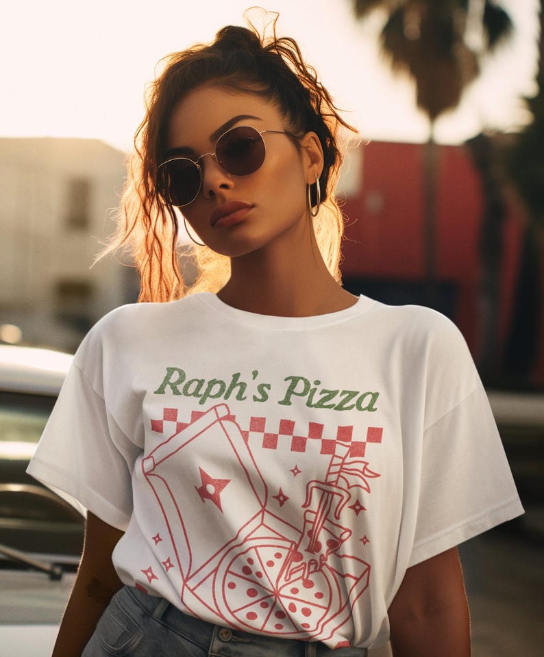 May include: White t-shirt with a graphic of a pizza box and a pizza slice with the text "Raph's Pizza" in green and red lettering.