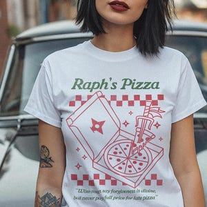 May include: White t-shirt with a red and white pizza box graphic and the text "Raph's Pizza". The pizza box is open and a pizza slice is being pulled out with a sword. The text below the graphic says "Wise man say forgiveness is divine, but never pay full price for late pizza."