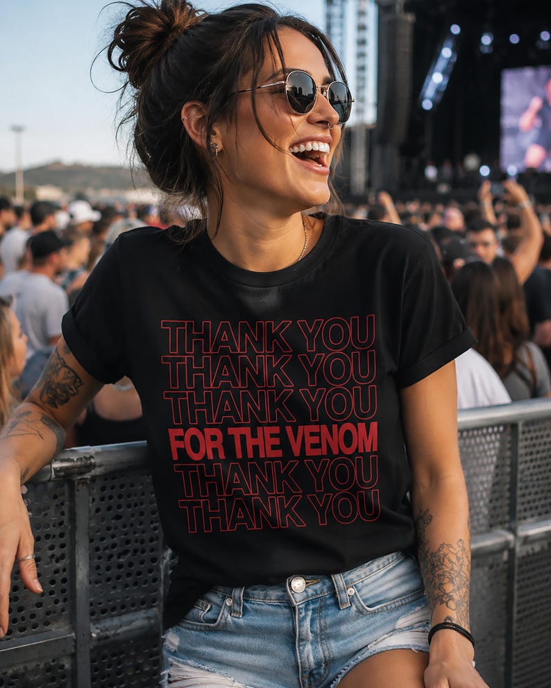 Pu&ograve; includere: T-shirt nero con la scritta "THANK YOU THANK YOU THANK YOU FOR THE VENOM THANK YOU THANK YOU" in rosso. La maglietta &egrave; indossata con pantaloncini di jeans blu. La persona sorride e indossa occhiali da sole.