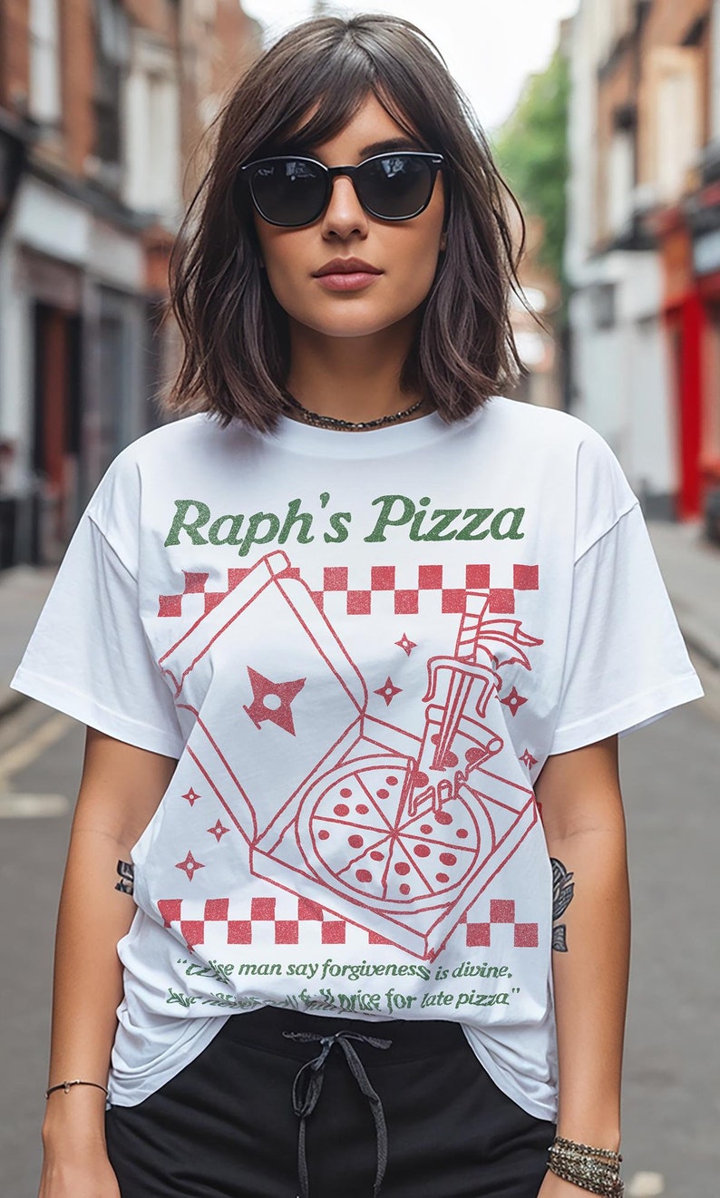 May include: White t-shirt with a green and red graphic of a pizza box with a pizza inside. The text "Raph's Pizza" is printed in green on the shirt. The quote "'Cause man say forgiveness is divine, the price for late pizza." is printed in black below the graphic.