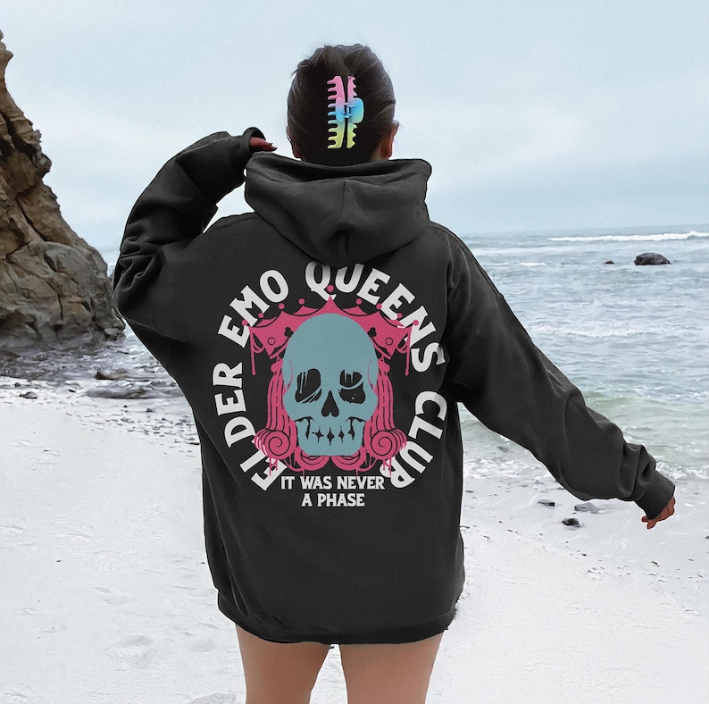May include: Black hooded sweatshirt with a pink and blue graphic print of a skull with the text "Elder Emo Queens Club" and "It was never a phase".