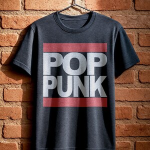 May include: Dark gray t-shirt with the words "POP PUNK" in white block letters, set against a red rectangular background. The shirt is hanging on a black hanger against a brick wall.
